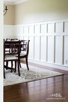 a dinning room table and chairs in front of white paneled walls with wainscoting