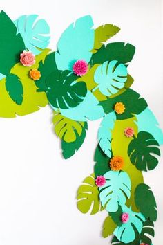 paper flowers and leaves are hanging on the wall in front of a white background,