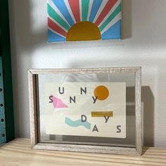 a wooden table topped with a framed sign and a painting on the wall behind it