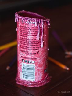 a pink can sitting on top of a wooden table next to colored crayons