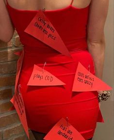 a woman in a red dress has her back to the camera and is holding up several pieces of paper with words written on them