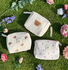 three small purses sitting on top of a lush green field next to pink flowers