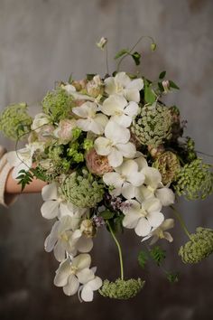 a bouquet of white flowers and greenery is held by a woman's arm