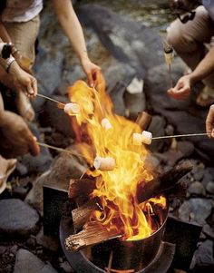 people roasting marshmallows over an open fire with tongs in their hands