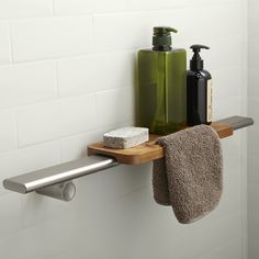 a bathroom shelf with soap and lotion on it next to a towel rack in front of a white tiled wall