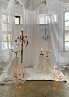 several candles are lit on the floor in front of a curtained room with white drapes