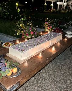 a table topped with a cake covered in frosting and surrounded by flowers, fruit and candles