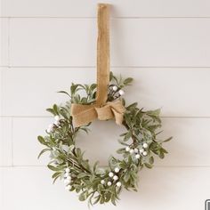 a wreath hanging on the wall with white flowers and greenery