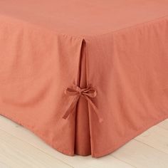 an orange bed skirt with a bow tied around the edge on a wooden floor in front of a white wall