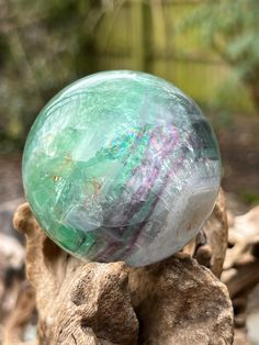 a green marble ball sitting on top of a wooden stump in front of some rocks