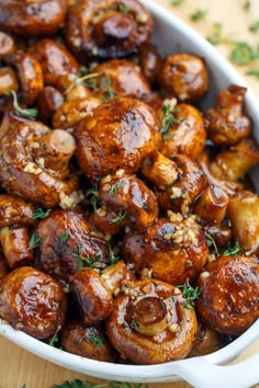 a white bowl filled with cooked mushrooms and garnished with herbs