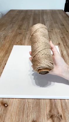 a person holding a roll of twine over a piece of paper on top of a wooden table