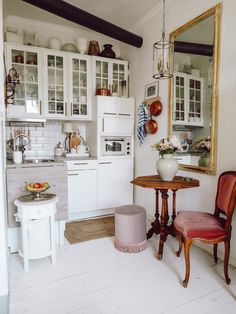 a small kitchen with white cabinets and wooden chairs in front of a table that has a vase on it