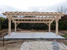 a wooden gazebo sitting on top of a cement slab in the middle of a yard