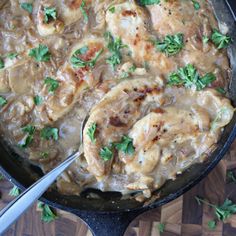 a skillet filled with chicken and gravy on top of a wooden table