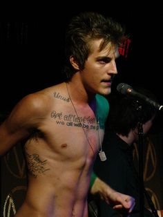 a shirtless man standing in front of a microphone with tattoos on his chest and arm