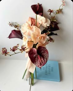 an arrangement of flowers in a vase on top of a white table next to a blue book