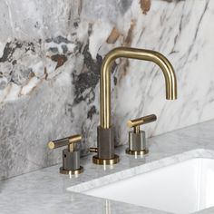 two faucets on a marble counter top next to a white sink with gold handles