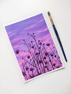 a painting of purple flowers on a white surface next to a blue and gold brush