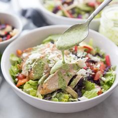 a salad with dressing being drizzled over it and topped with chicken, lettuce