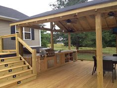 an outdoor kitchen with grill and stairs leading up to the back porch, next to a deck