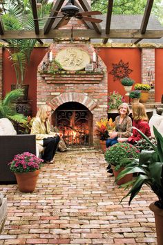 two women sitting on chairs in front of a brick fire place with potted plants