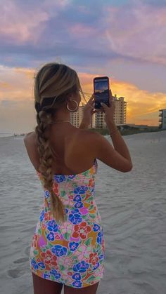 a woman standing on the beach taking a selfie with her cell phone at sunset