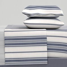 three pillows stacked on top of each other with blue and white striped sheets in the background