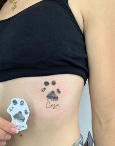 a woman with a dog paw tattoo on her stomach holding up a small sticker