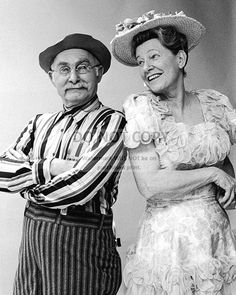 an old photo of two people dressed in fancy clothes and hats posing for the camera