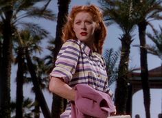 a woman with red hair is holding a purse and wearing a striped shirt in front of palm trees