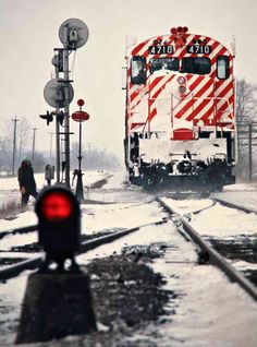 a red and white train traveling down tracks next to a snow covered street light on a snowy day