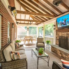 a covered porch with couches, chairs and a flat screen tv on the wall