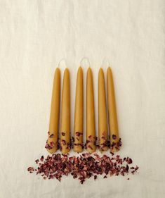 four candles with dried flowers on top of them next to some petals and other items