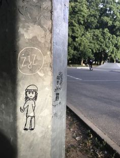 graffiti on the side of a pole next to a street with trees in the background