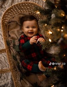 a baby sitting in a basket next to a christmas tree