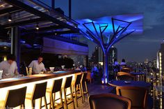 people are sitting at the bar on top of a building in front of cityscape