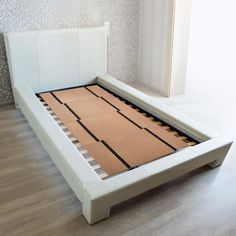 a white bed frame with wooden slats on the top and bottom sides, in front of a window