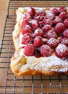 a pastry covered in powdered sugar and raspberries on a wire cooling rack