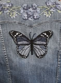 a butterfly is on the back of a jean jacket with floral appliques