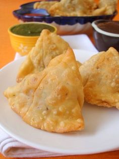 three fried pastries on a white plate with dipping sauces in the back ground