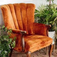 an orange chair sitting next to a potted plant on top of a brick floor