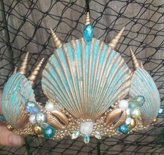 a hand holding a blue and gold tiara with seashells on it's sides