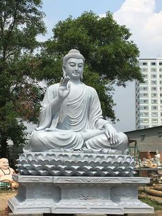 a large buddha statue sitting on top of a cement bench in front of a tree