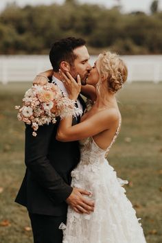 a bride and groom kissing in front of a white fence with flowers on the grass