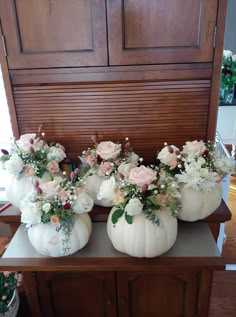 four white pumpkins with flowers in them sitting on a table