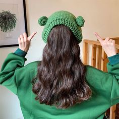 a woman with long hair wearing a green knitted hat and pointing fingers to the side