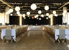 a banquet hall with tables and chairs covered in white tablecloths, lights and paper lanterns