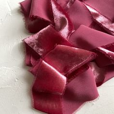 a pile of pink satin ribbon on top of a white tablecloth covered in small pieces of fabric