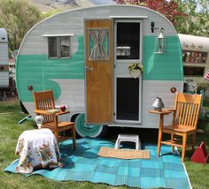 an rv is parked in the grass with two chairs and a table next to it